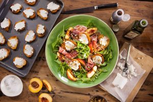 Mediterranean-inspired salad with prosciutto, peach, rocket, and goats cheese croutés, dressed in the best tasting olive oil for a healthy recipe.